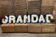 blued & white funeral letters, spelling Grandad with red rose detailing spays.