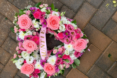 Pink open heart funeral wreath in a mix of pink flowers. Finished with a pink Auntie sash.