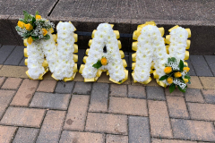 yellow & white funeral letters, spelling Nan, with yellow ribbon edging & yellow rose sprays.