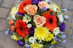 Bight funeral posy in a mix of yellow, orange, purple & peach flowers.