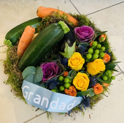 Funeral tribute with an allotment design in mind. A flat round posy pad with seasonal vegetables and flowers.