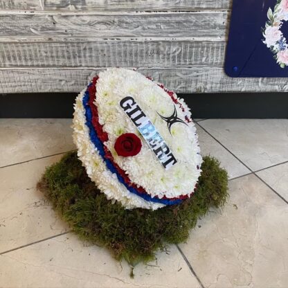 Funeral Rugby Tribute in the shape of a rugby ball covered in white chrysanthemums and your own choice of club colours and emblems.