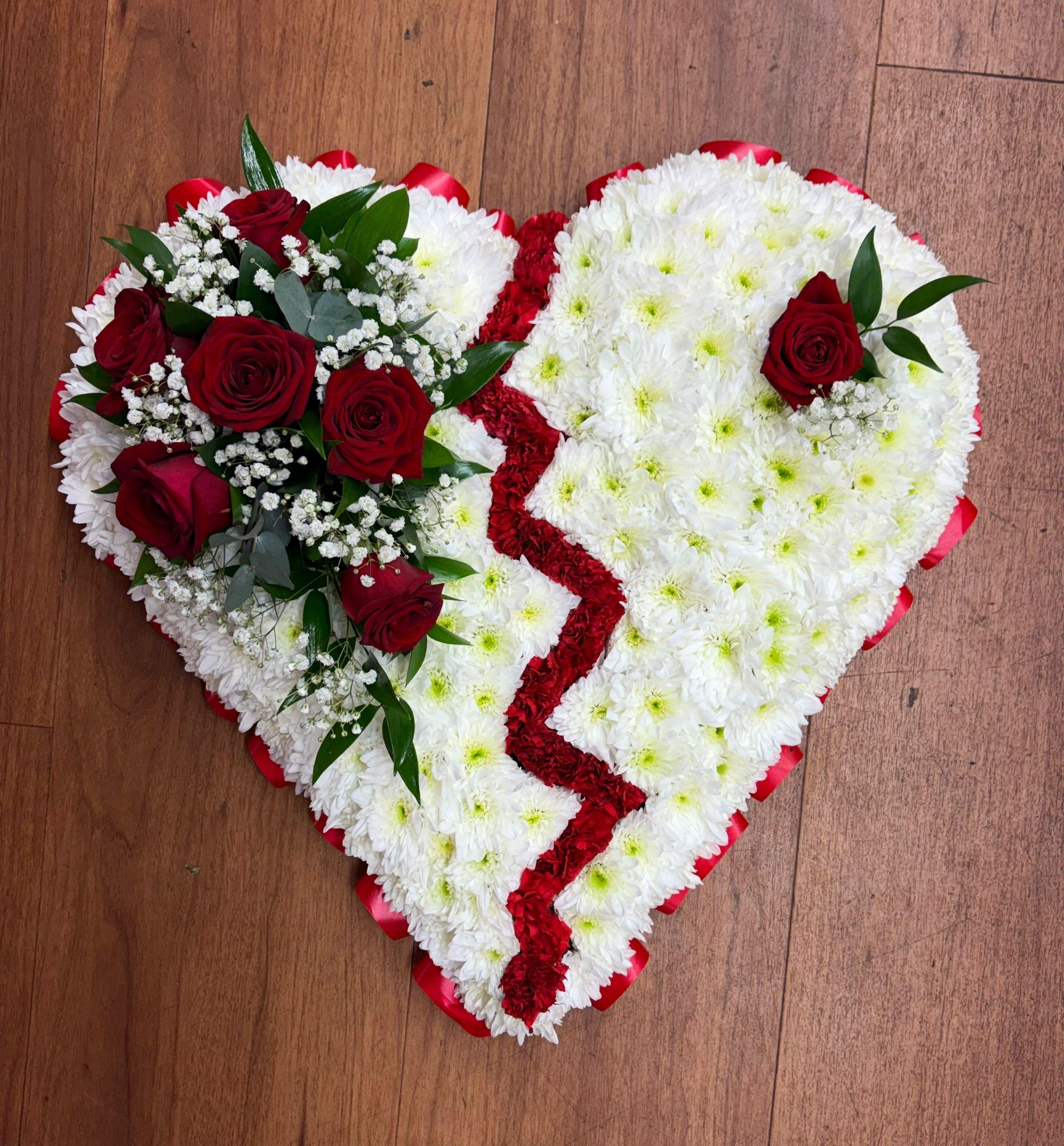 White based flowers with red broken line design down middle of the heart. Red roses, gyp and greenery spray on left side and single red rose on other side. Red ribbon around the heart.